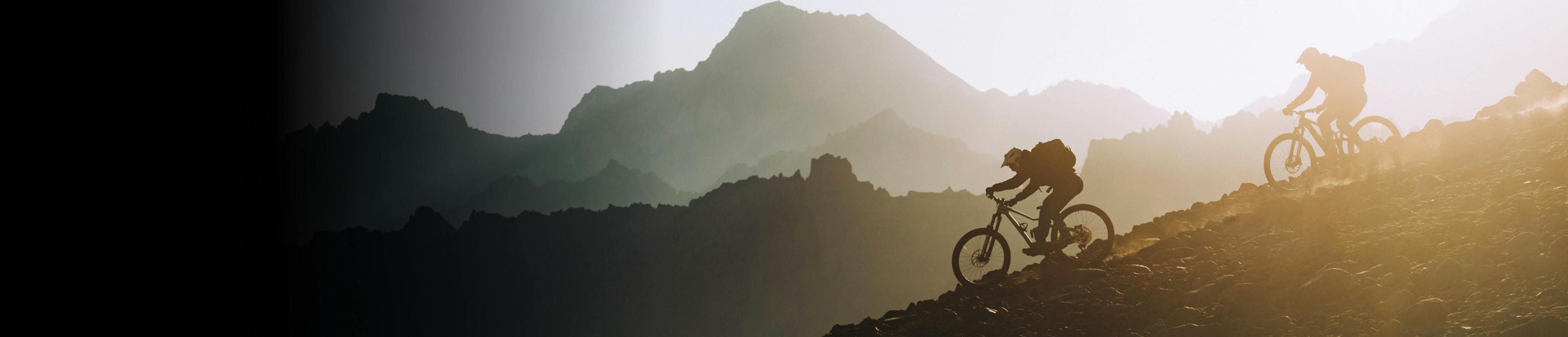 Two bikers riding down a mountain during sunset.