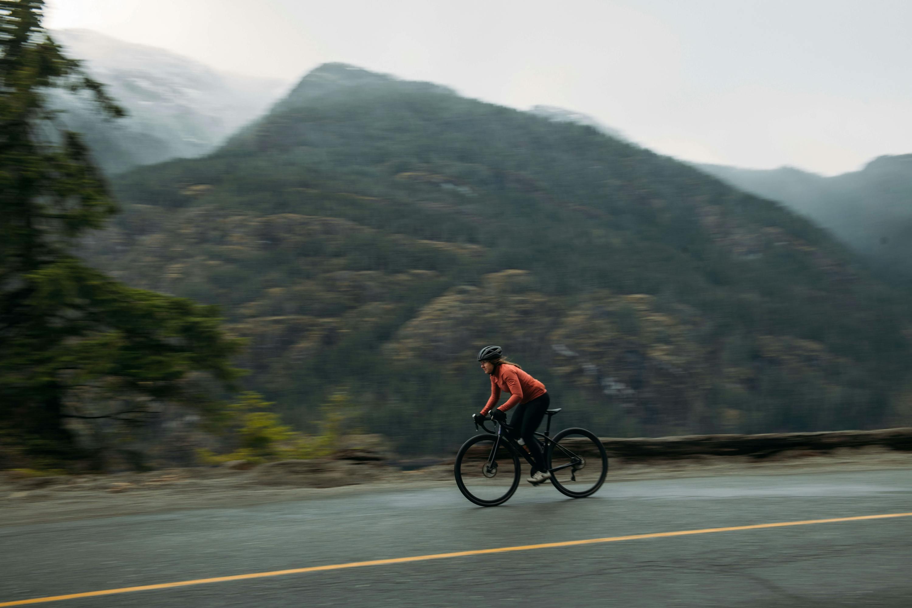 Woman riding a bike on the road with mountains in the back.