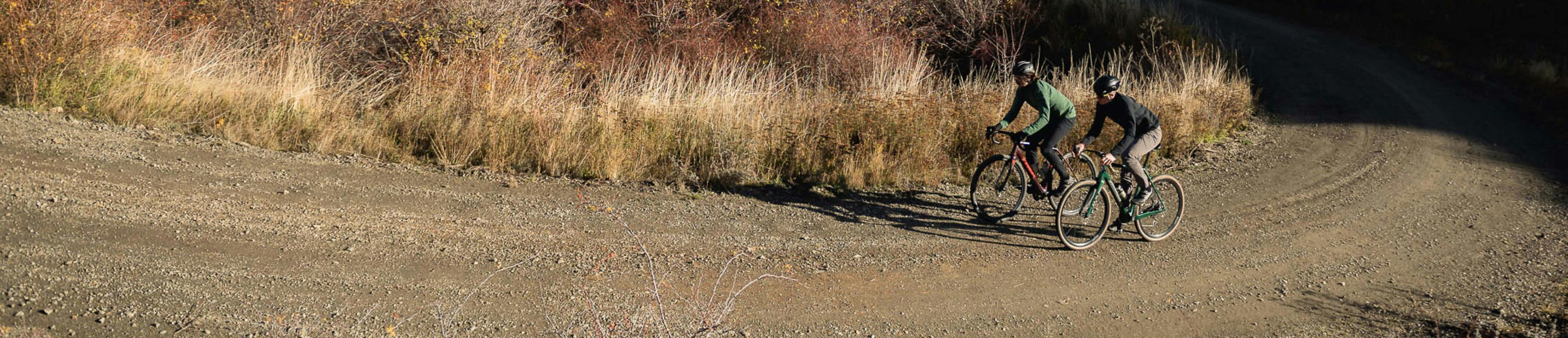 Two people riding a bike on a gravel road