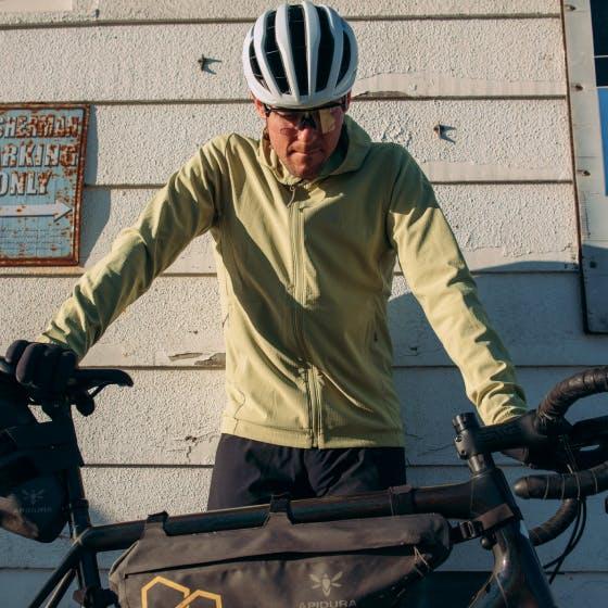 Man in yellow jacket with a bike in front of him looking down